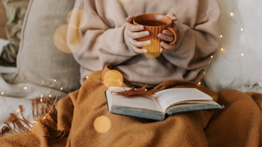 Femme qui lit un livre avec une bonne tasse de thé et un plaid bien douillet