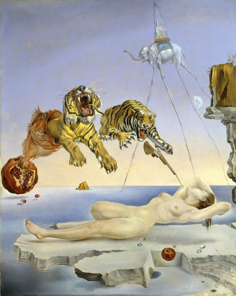 Image du tableau de Dali "Une seconde avant l'éveil". On y voit deux tigres surgissant d'un poisson lui meme surgissant d'une grenade, fonçant sur une femme nue endormie laçivement. Elle semble flotter sur un bout de terre au milieu de l'océan, en fond, on aperçoit un éléphant aux pattes qui ressemblent à des fils de fer.