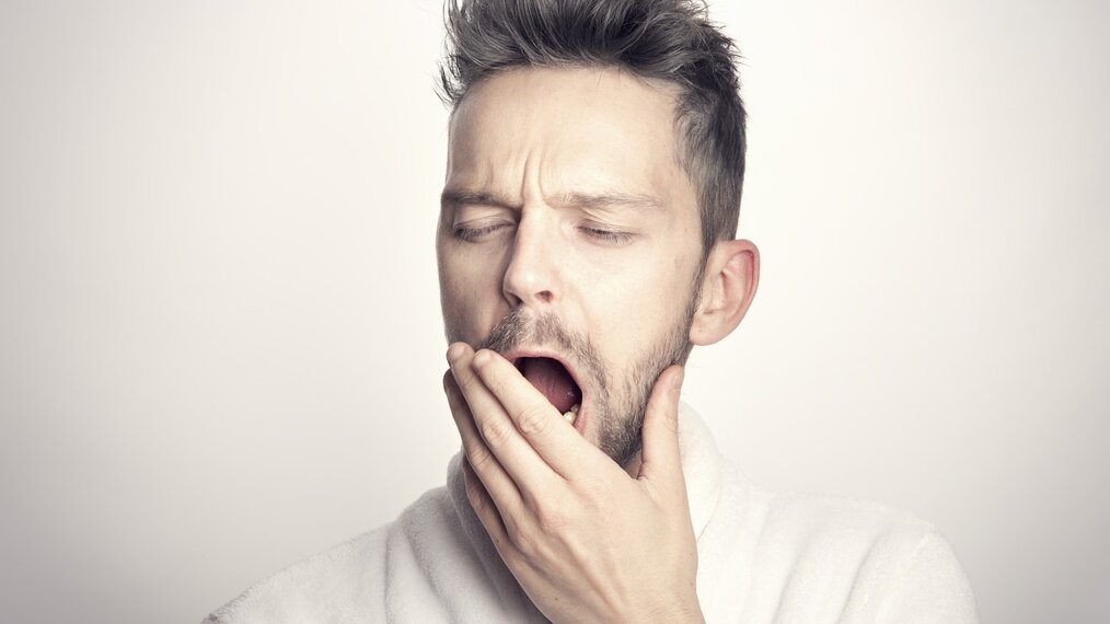 Un homme bâille avec sa main devant la bouche.