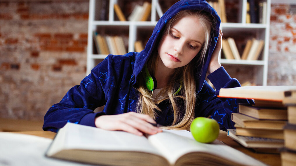 Une jeune fille es en train de réviser. Un livre est grand ouvert devant elle.